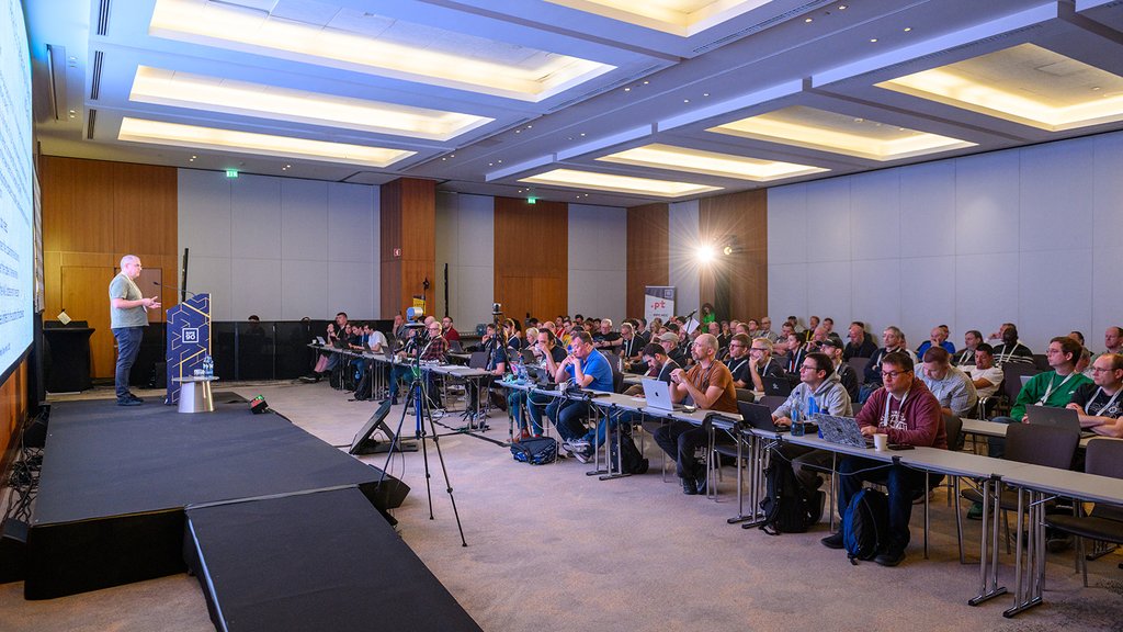 An audience watches a man present on stage.