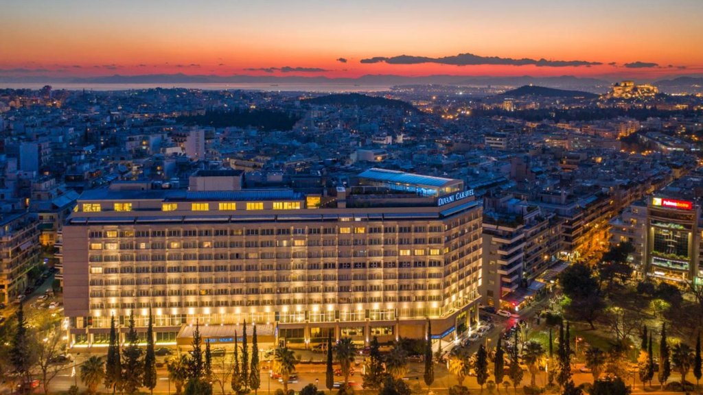 Aerial view of a large hotel with a city in the background as the sun is setting.